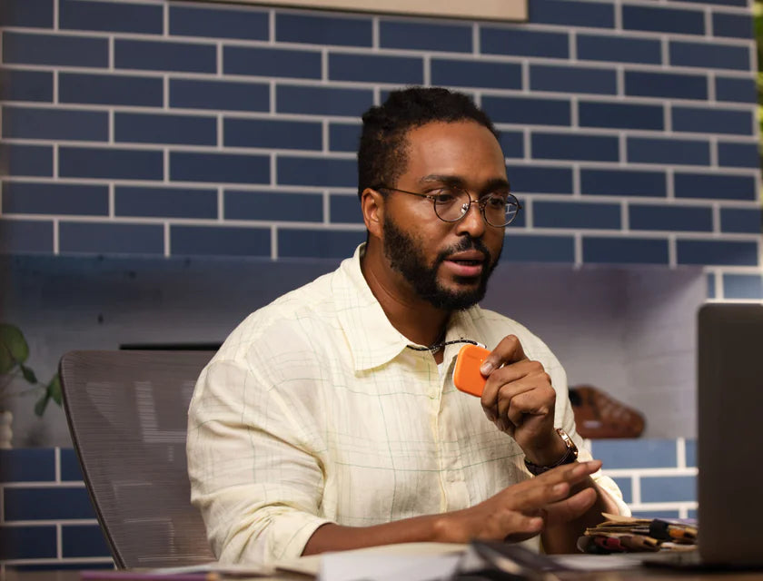Man holding an orange SpeakON device beside a laptop